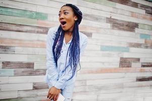 menina afro-americana elegante com dreads segurando o celular na mão, ao ar livre contra a parede de madeira. foto