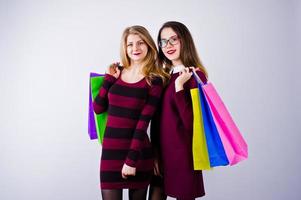 duas amigas lindas em vestidos de cereja posando com sacolas multicoloridas no estúdio. foto