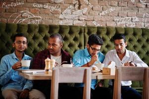 grupo de quatro homens do sul da Ásia posou na reunião de negócios no café. índios assistindo tv e torcendo pelo seu time favorito. foto