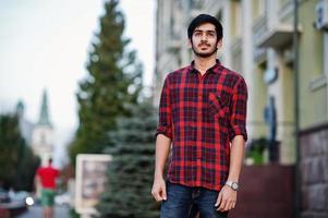 homem jovem estudante indiano em jeans e camisa xadrez vermelha posou na cidade. foto