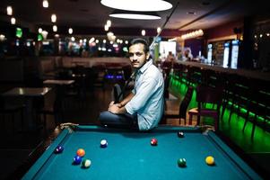 homem árabe elegante usa jeans jogando bilhar no bar. foto