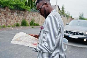 homem afro-americano rico e elegante de blazer e óculos lê revista contra seu carro suv. foto