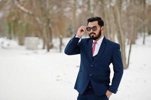 homem de negócios de barba indiana elegante de terno e óculos de sol posou em dia de inverno ao ar livre. foto