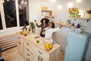 duas amigas afro-americanas mulheres passando tempo na cozinha com vinho. namoradas negras relaxando em casa. foto