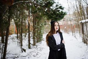 modelo morena de pernas longas na moda no manto preto longo e chapéu ao ar livre no dia de inverno. foto