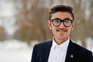 feche o retrato do homem estudante indiano elegante de terno e óculos posou no dia de inverno ao ar livre. foto