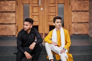 dois amigos indianos elegantes em roupas tradicionais posaram ao ar livre e sentados nas escadas. foto