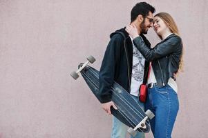 legal casal multirracial posando contra a parede rosa com longboard. foto