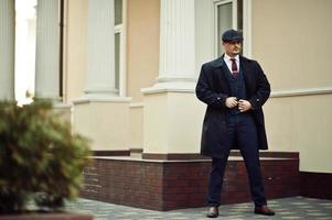 retrato de homem de negócios árabe inglês dos anos 20 retrô vestindo casaco escuro, terno, gravata e boné liso. foto