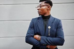 homem afro-americano incrivelmente bonito usa blazer azul com broche, gola alta preta e óculos posados na rua. negro na moda. foto