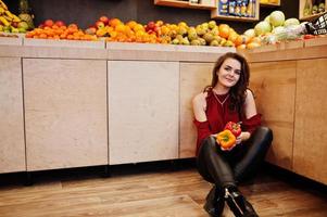 garota de vermelho segurando duas pimentas na loja de frutas. foto