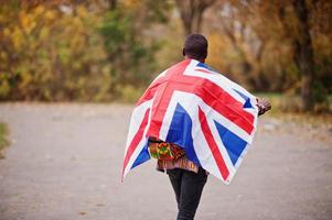 homem africano na camisa tradicional da África no parque outono com bandeira da Grã-Bretanha. foto