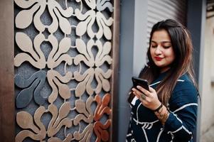 mulher indiana morena de vestido longo elegante posou ao ar livre com o celular na mão. foto