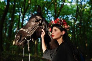 garota mística em grinalda veste em preto com cavalo em madeira. foto