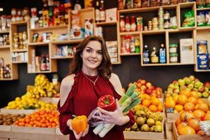 garota de vermelho segurando diferentes vegetais na loja de frutas. foto