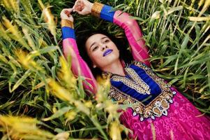 tenra garota indiana em saree, com lábios violeta compõem posou no campo no pôr do sol. modelo elegante da índia. foto