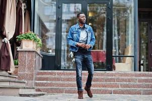 modelo de homem afro-americano sério atraente jovem. cara bonito moderno em pé de jaqueta jeans na rua urbana da cidade. foto