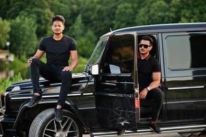 dois irmãos asiáticos vestem todo preto posando perto do carro suv. foto