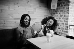 Atraente afro-americano duas amigas sentadas no café com café com leite e sinal reservado. foto