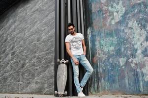 homem árabe de estilo de rua em óculos com longboard posou. foto