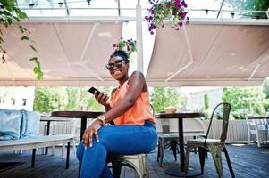 garota afro-americana sentada na mesa de caffe com telefone celular. foto