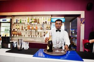 barman americano africano no bar segurando champanhe com copos na bandeja. foto