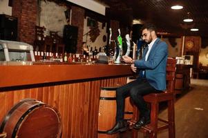 homem árabe bem vestido bonito com copo de uísque e charuto posou no pub. foto