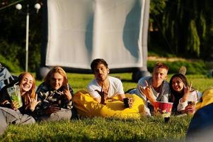 jovem grupo multiétnico de pessoas assistindo filme no poof no cinema ao ar livre. foto