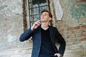 jovem macho vestindo jaqueta elegante blac fumando cigarro nas ruas. foto