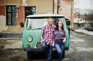 casal elegante usa camisa quadriculada apaixonada juntos contra a velha minivan. foto