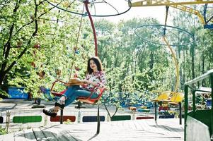 retrato de menina morena de óculos cor de rosa e chapéu com sorvete no parque de diversões. foto