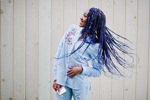 menina afro-americana elegante com dreads segurando o celular na mão, ao ar livre contra a parede de madeira em tempo de neve. foto