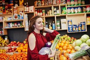 garota de vermelho segurando diferentes vegetais na loja de frutas. foto