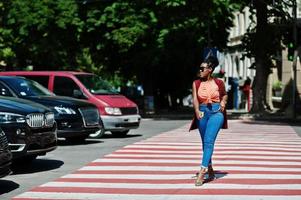 elegante mulher afro-americana andando na faixa de pedestres ou travessia de pedestres com o celular na mão. foto