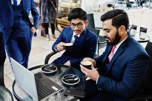 dois homens de negócios indianos de terno sentado no escritório no café, olhando para o laptop e tomando café. foto
