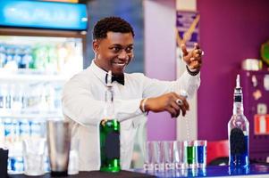 barman americano africano no bar fazendo coquetéis em tiros. preparação de bebidas alcoólicas. foto