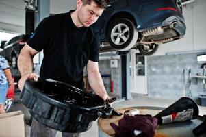 tema de reparação e manutenção de automóveis. mecânico de uniforme trabalhando em auto serviço, despejando óleo de motor velho em barril. foto