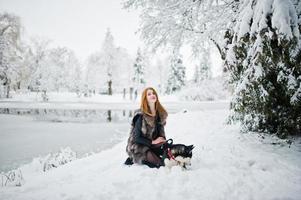 garota ruiva andando no parque com cachorro husky em dia de inverno. foto