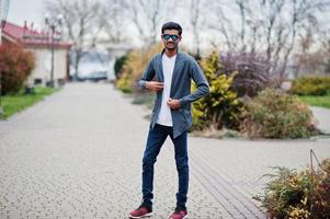 homem indiano elegante em óculos de sol usa casual posou ao ar livre. foto