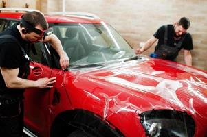 trabalhador de serviço de carro colocou filme anti cascalho em um corpo de carro vermelho na oficina de detalhamento de veículos. proteção do carro com películas especiais. foto