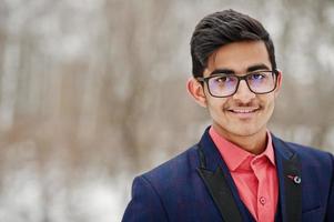 Feche o retrato do homem elegante estudante indiano de terno, óculos posou no dia de inverno ao ar livre. foto