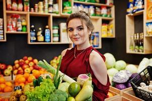 garota de vermelho segurando diferentes vegetais na loja de frutas. foto