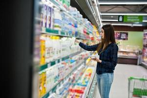 mulher de compras olhando para as prateleiras do supermercado. retrato de uma jovem em uma loja de mercado segurando a produção de leite. foto