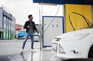 homem do sul da Ásia ou homem indiano lavando seu transporte branco na lavagem de carros. foto