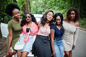 grupo de cinco garotas afro-americanas felizes sentadas em um capô de carro. foto