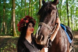 garota mística em grinalda veste em preto com cavalo em madeira. foto