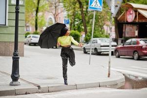 retrato de uma jovem bela mulher afro-americana segurando o guarda-chuva preto tentar pegar um táxi. foto