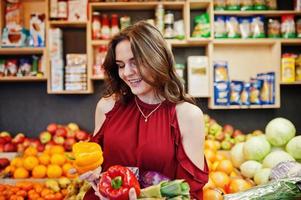 garota de vermelho segurando diferentes vegetais na loja de frutas. foto