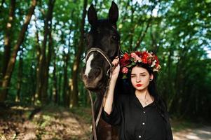 garota mística em grinalda veste em preto com cavalo em madeira. foto