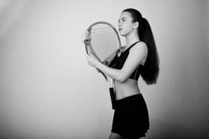 retrato preto e branco do jogador de mulher jovem e bonita em roupas esportivas, segurando a raquete de tênis em pé contra um fundo branco. foto